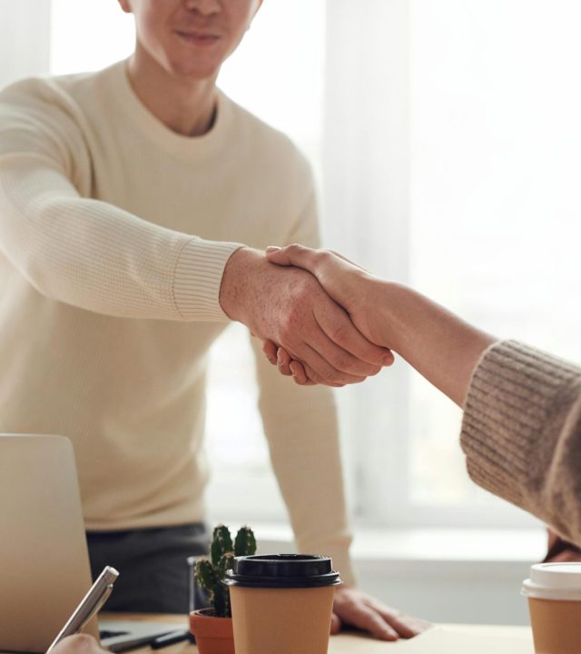 Close-up of professionals shaking hands over coffee in a modern office.